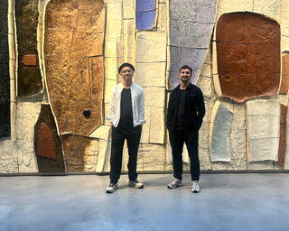 Two people standing in front of a large abstract wall sculpture.